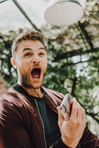 Excited young man shouting while holding mobile phone