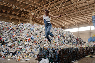 Full length of young woman jumping against garbage heap