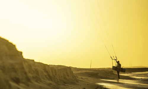 Man kiteboarding at beach against clear sky during sunset