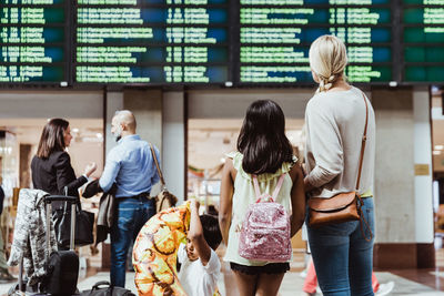 Family and business colleagues looking at arrival departure board while waiting in station