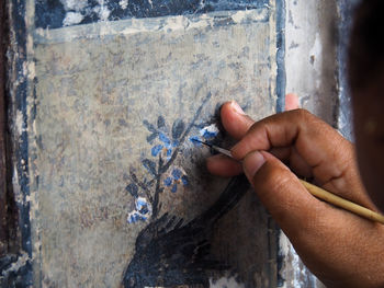 Close-up of hand holding painting against wall