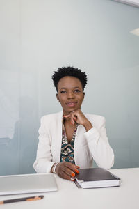 Confident young businesswoman with diary sitting at desk in office