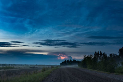 Dirt road amidst field against sky