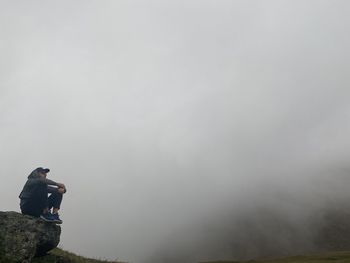 Full length of man sitting on rock against fog