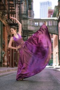 Full length of young woman dancing on street amidst buildings in city