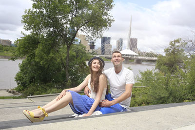 Young couple sitting on tree against plants