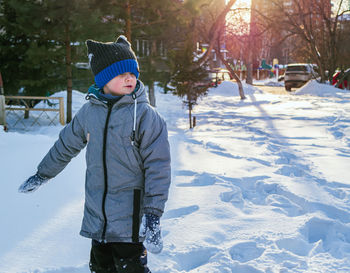 Smiling caucasian boy in green jacket and blue knit cap is standing on the snow.