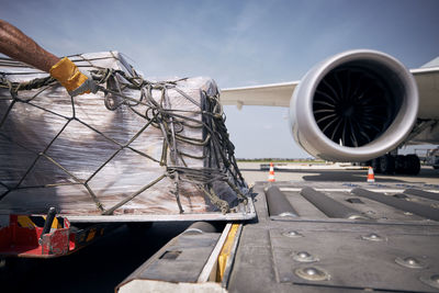 Hand of ground crew during unloading freight airplane. cargo containers against jet engine of plane.