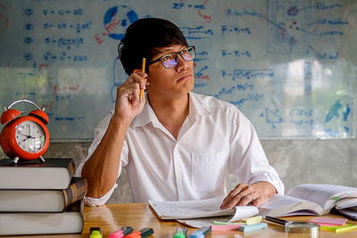 Young man studying with school supplies on table at home