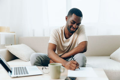 Young man using laptop while sitting on bed at home