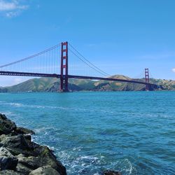 Suspension bridge over sea against blue sky