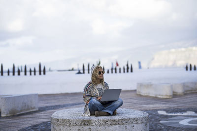 People sitting on rock by sea against sky