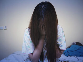 Close-up of woman covering face while sitting on bed