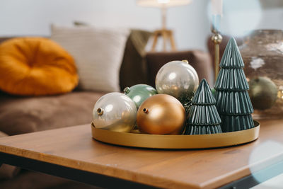 Christmas decor on the table of livingroom. baubles and christmas small toy trees on tray by sofa in