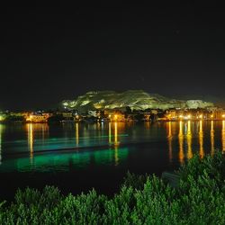 Reflection of illuminated trees in water against sky at night