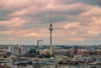 Fernsehturm amidst cityscape during sunset