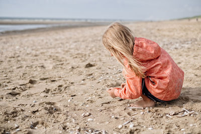 Side view of girl playing with sand at beach