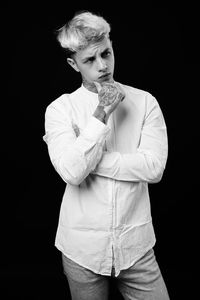 Portrait of young man standing against black background