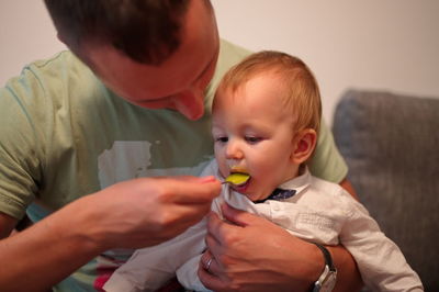 Father sitting on a sofa and feeding his cute little baby