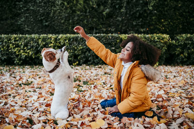Woman with dog sitting on leaves during autumn