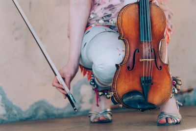 Low section of woman holding violin while crouching on floor