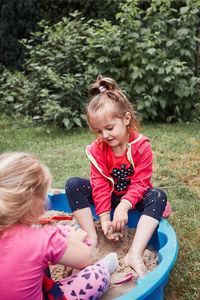 High angle view of girls playing with sand while sitting on grass