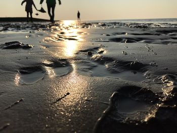 Low section of wet beach against sky during sunset