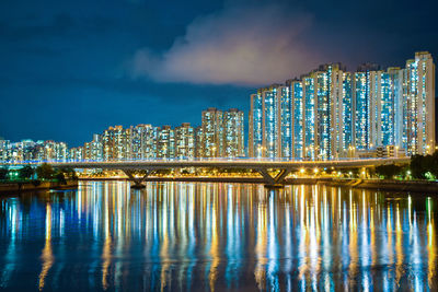 Illuminated modern buildings by river against sky at night