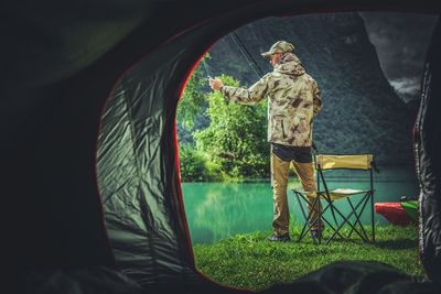 Man fishing in lake seen through tent
