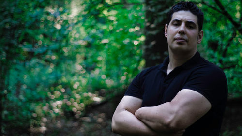 Portrait of muscular man standing against trees