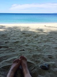 Low section of woman relaxing at beach against sky