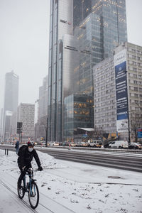 Man riding bicycle on city street against modern buildings