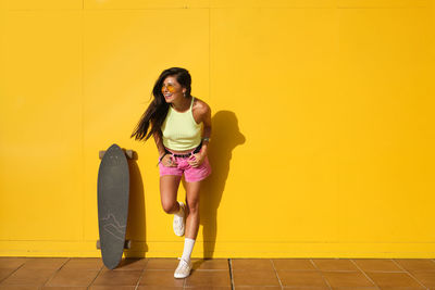 Portrait of smiling young woman standing against yellow wall