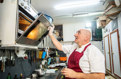 Older adult opening an oven in the kitchen of a bakery in serbia