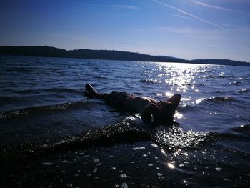 Person laying in sea against sky