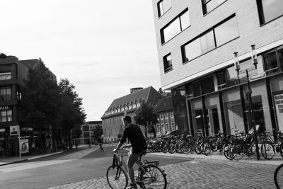 Man riding bicycle in city against sky