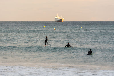 People on sea against sky during sunset