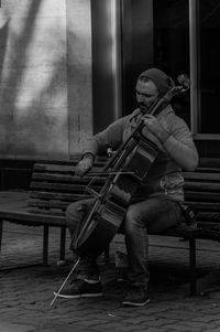 Street musician playing cello on bench