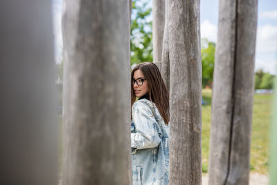 Portrait of young woman standing on tree trunk