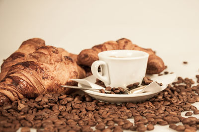 Close-up of cup and roasted coffee beans against white background