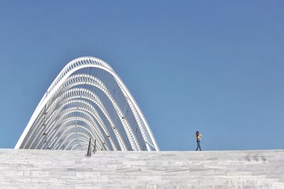 Woman standing by modern built structure against clear blue sky