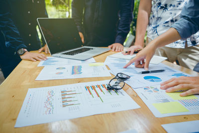 Midsection of coworkers discussing graphs on desk in office