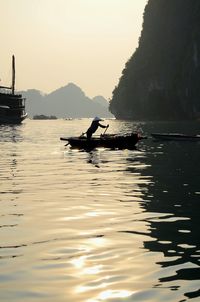 Silhouette woman sailing in sea against sky during sunset