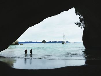 Silhouette people at beach seen through arch rock formation