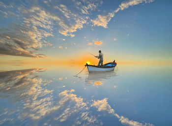 Man in boat on sea against sky during sunset