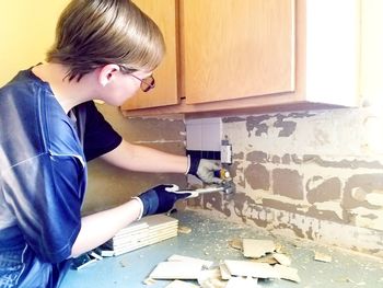 Woman removing tiles from wall