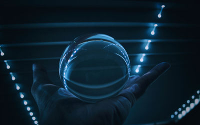 Cropped image of hand holding crystal ball against illuminated ceiling