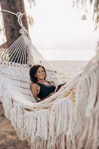 Portrait of smiling mature woman lying down in hammock at beach