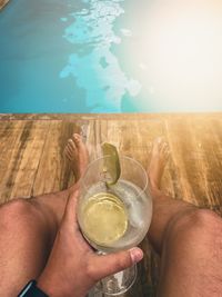 Midsection of man holding glass at swimming pool