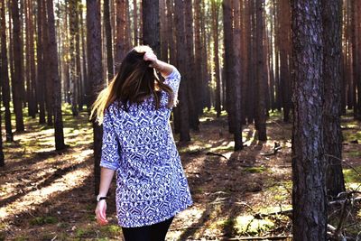 Rear view of woman standing on tree trunk in forest